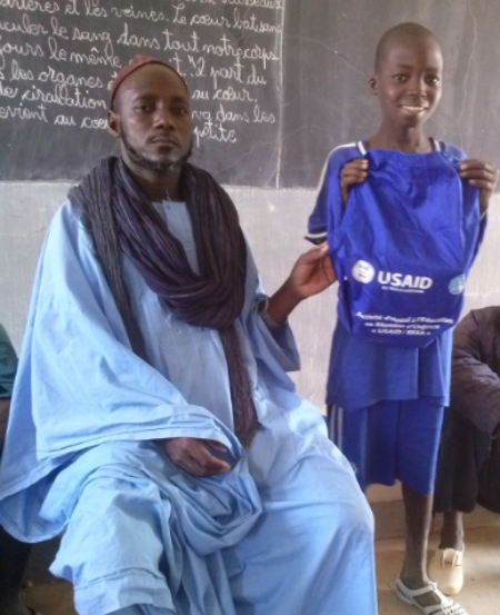 A photo showing a student smiling and holding up the kit he received