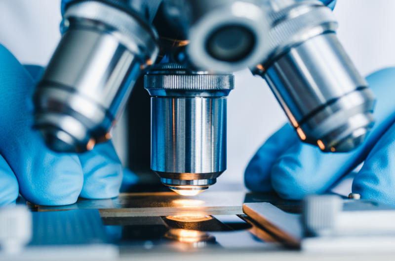 A close-up of a scientist placing a sample under a microscope lens.