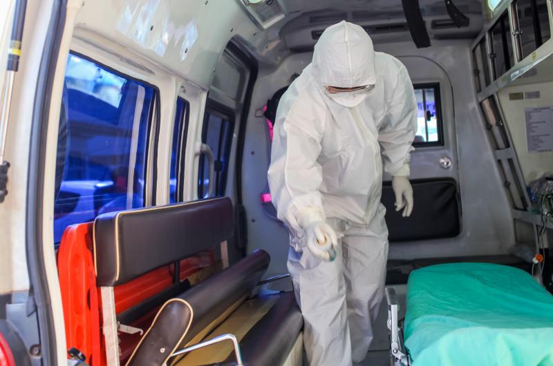 A medical specialist, dressed in personal protective equipment (PPE), who is standing in an ambulance.