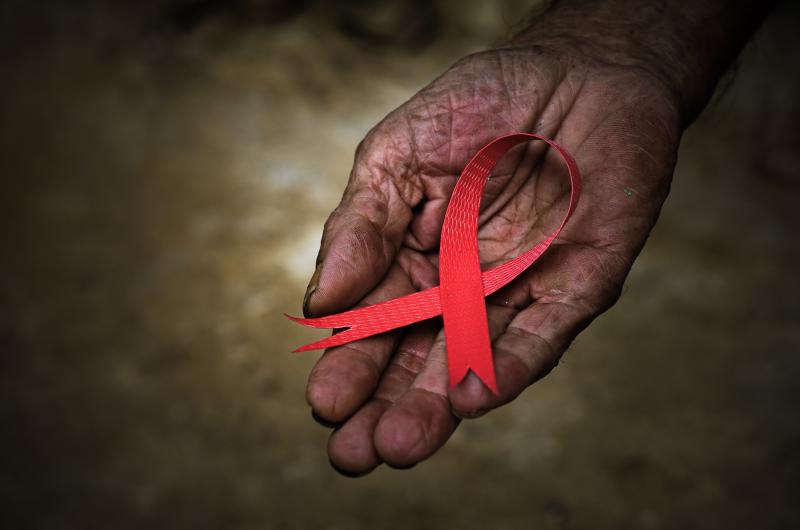 A close-up photo of a winkled hand holding an AIDS ribbon.