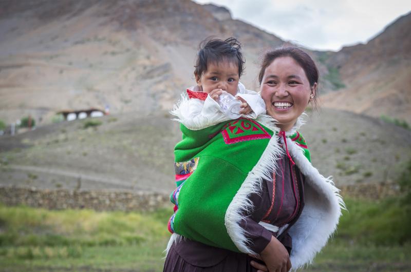 A women carrying a baby on her back while traversing Spiti Valley in India.