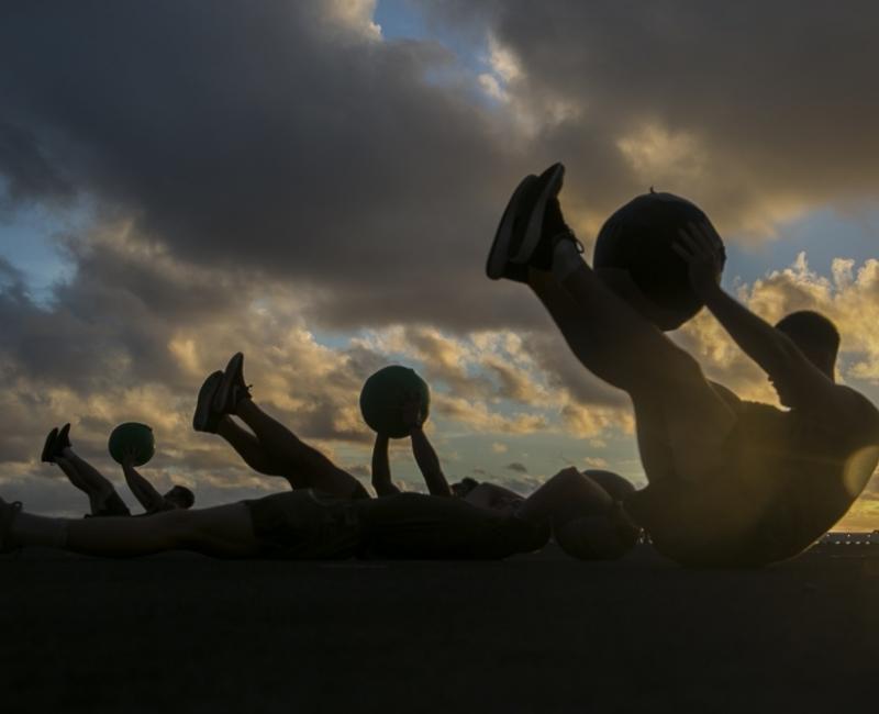 A silhouette of military professionals doing crunch exercises while holding a ball.